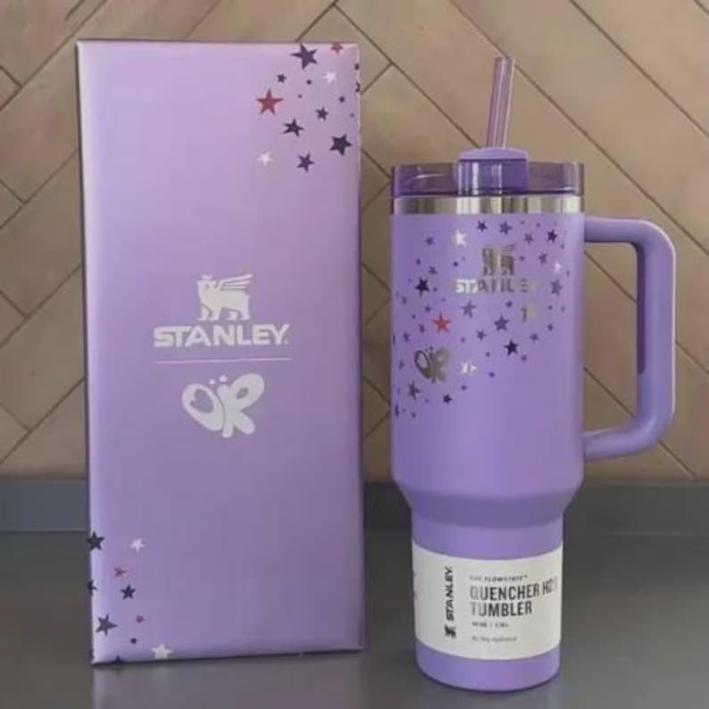 May include: A lavender Stanley Quencher H2.0 Flowstate tumbler with a handle and straw, next to a matching box. Both the tumbler and box feature star and butterfly designs. The tumbler has a capacity of 40 oz / 1.18L.