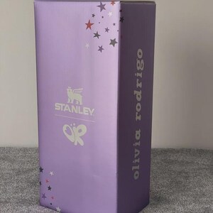 Peut inclure: Une bo&icirc;te rectangulaire haute de couleur violet clair. La bo&icirc;te pr&eacute;sente le logo "STANLEY" et le nom "olivia rodrigo" en lettres argent&eacute;es. Des &eacute;toiles d&eacute;coratives rouges, grises et blanches ornent la bo&icirc;te.
