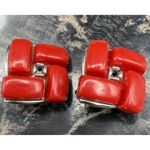 May include: A pair of vintage clip-on earrings. Each earring features a cluster of four rectangular, glossy, red stones set in a silver-tone metal frame. The earrings have a geometric design and a retro aesthetic.