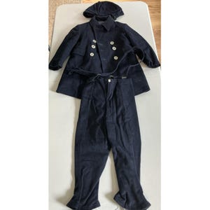 May include: A navy blue vintage sailor suit set, including a double-breasted coat with white buttons, matching pants, and a hood. The coat has a belt. The set is displayed on a light-colored surface.