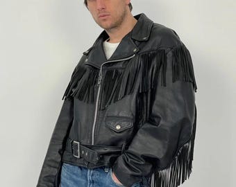 May include: A black leather motorcycle jacket featuring long fringe detailing across the chest, back, and sleeves. The jacket includes a silver-toned front zipper, a snap-button pocket, a waist belt with a metal buckle, and a wide lapel collar.
