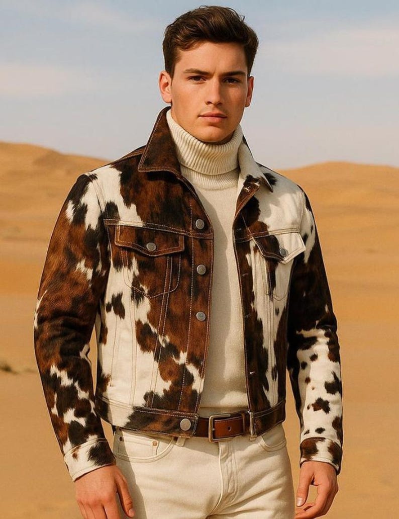 May include: A brown and white cowhide-patterned jacket with a classic collar and buttoned pockets. The jacket is paired with a cream-colored turtleneck sweater, light-colored jeans, and a brown leather belt. The background is a desert landscape.