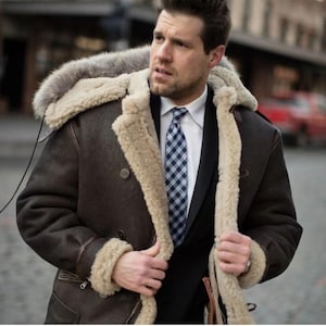 Peut inclure: Un manteau en peau de mouton marron avec une capuche doublée de fourrure. Le manteau a un design croisé et une doublure en peau de mouton de couleur crème. La personne porte une chemise blanche et une cravate à carreaux bleus et blancs. Un vêtement d'extérieur élégant.