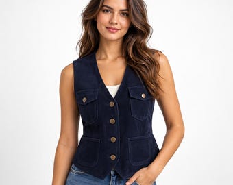 May include: A dark navy blue sleeveless vest featuring a V-neckline, a front button closure with metallic buttons, two chest pockets with buttoned flaps, and two lower patch pockets. The garment is constructed from a soft, suede-like material.
