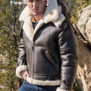 Peut inclure: Veste en cuir marron avec doublure en peau de mouton blanche et capuche bordée de fourrure. La veste est dotée d'une fermeture éclair, d'une poche poitrine et d'une ceinture à la taille. Les poignets et le col sont également doublés de peau de mouton blanche.