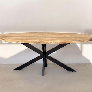 Op de afbeelding: Ovale eettafel met een lichtbruin houten blad. De tafel heeft een zwart metalen onderstel met een stervormig ontwerp. De tafel is een modern ontwerp en is geschikt voor een eetkamer of keuken. De tafel is ongeveer 180 cm lang.