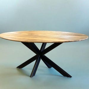 Peut inclure: Une table de salle à manger ovale en bois avec un plateau brun clair et une base en métal noir en forme d'étoile. La table mesure environ 152 cm de diamètre, idéale pour une salle à manger ou une cuisine.
