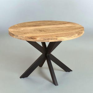 Puede incluir: Una mesa redonda de madera con una encimera texturizada de color marrón claro. La mesa tiene una base de metal marrón oscuro con forma de estrella. La mesa tiene unos 91 cm de diámetro.