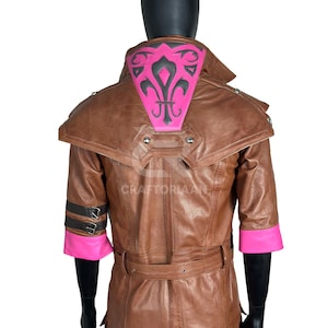 Può includere: Giacca in pelle marrone con un design rosa e nero sul retro. La giacca ha una cintura, maniche corte con polsini rosa e borchie decorative in metallo. Il retro presenta un design a giglio rosa e nero.