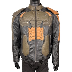 May include: A multi-colored leather jacket featuring a black base with olive green and tan accents. The jacket includes a stand-up collar, a full-length front zipper, structured shoulder padding, and a segmented tan panel design on the chest.