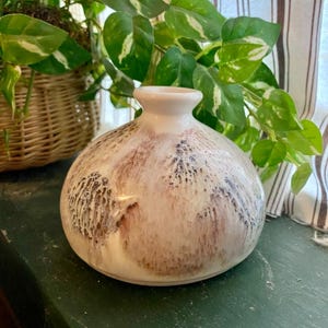 May include: A white ceramic vase with a round body and a brown and white speckled glaze.