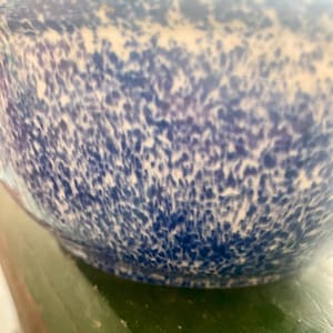 May include: A blue and white speckled ceramic bowl. The bowl has a rounded shape and a speckled pattern of dark blue spots on a white background. The bowl is likely used for serving food or as a decorative item.