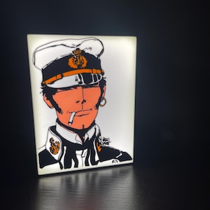 Könnte beinhalten: Rechteckiges, beleuchtetes Kunstwerk mit einer stilisierten Darstellung eines Marineoffiziers, der raucht. Das Kunstwerk verwendet Orange, Schwarz und Gold vor einem weißen Hintergrund. Der Offizier trägt eine weiße Mütze mit goldenem Emblem.