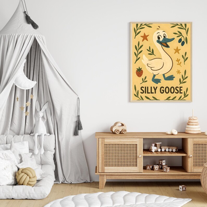 May include: A framed print featuring a cartoon goose with the text "SILLY GOOSE" on a yellow background. The goose is white with a blue beak and feet, surrounded by green leaves, stars, and a strawberry. The artwork is displayed in a child's room.