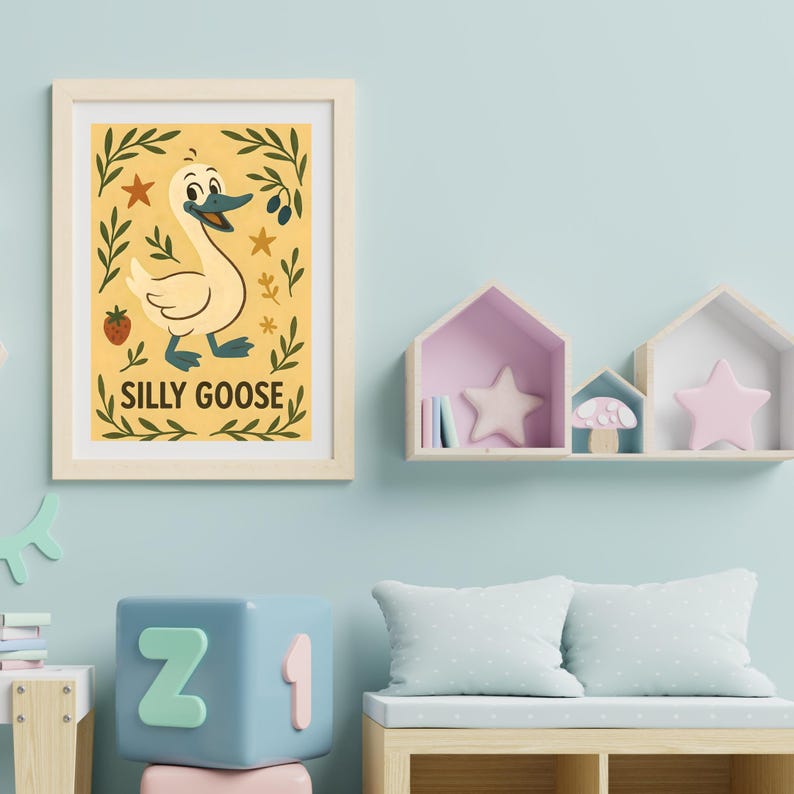 May include: A framed print featuring a whimsical illustration of a goose with the text "SILLY GOOSE". The artwork has a yellow background with decorative leaves, stars, and a strawberry. The frame is a light wood color.