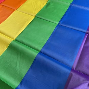 May include: A rainbow pride flag with six horizontal stripes in the colors red, orange, yellow, green, blue, and purple. The flag is folded in a diagonal pattern.