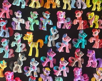 Könnte beinhalten: Eine große Sammlung kleiner Pony-Figuren aus Kunststoff in verschiedenen Farben wie Pink, Blau, Gelb, Grün und Lila. Jedes Pony hat eine einzigartige Mähne und einen Schweif, einige mit Flügeln oder Horn-Details, angeordnet in einer Gruppe.