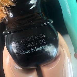 May include: Close-up of a doll's backside, featuring a black swimsuit bottom. The doll's skin is a light tan color. The text "&copy; 2013 Mattel 1186 MJ, 1, NL Made in Indonesia" is printed on the swimsuit bottom.