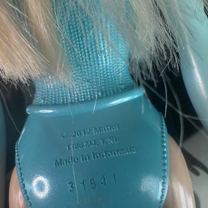May include: Close-up of a doll's back, featuring a light blue swimsuit and blonde hair. The text on the doll reads "&copy; 2012 Mattel, Made in Indonesia" and the number "31541".