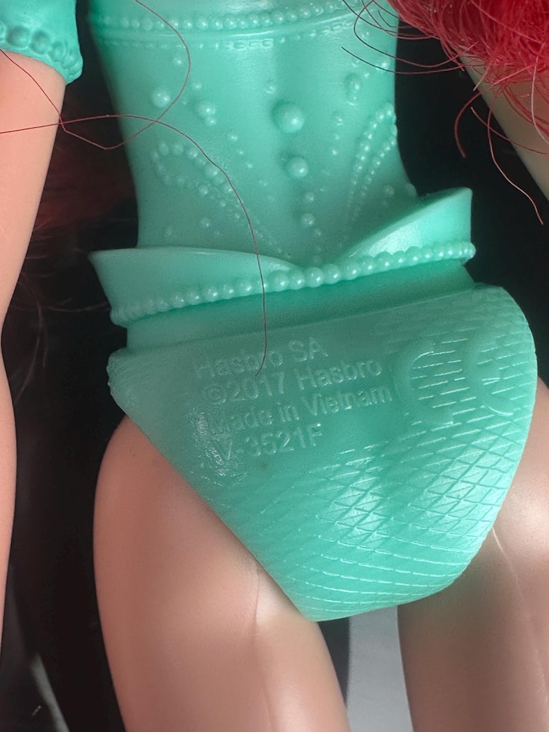 May include: Close-up of a turquoise doll's torso and legs. The doll's outfit includes a detailed bodice and a skirt-like bottom. The text "HASBRO SA &copy;2017 Hasbro Made in Vietnam" is printed on the doll's bottom.