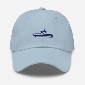 May include: Pale blue baseball cap featuring a navy blue boat outline embroidered on the front. The cap has a curved peak and an adjustable strap. A casual accessory for outdoor pursuits.