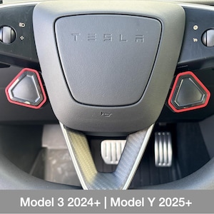 Może przedstawiać: Zbliżenie kierownicy Tesli z widoczną nazwą marki. Kierownica ma czarne i czerwone akcenty wokół elementów sterujących. Obraz zawiera tekst "Model 3 2024+ | Model Y 2025+" na dole.