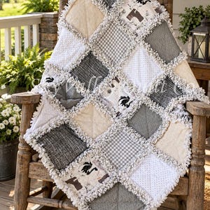 May include: A rag quilt featuring a patchwork design of square fabric blocks in shades of white, grey, and black. The quilt includes patterns such as gingham, polka dots, and solid textures, with frayed, exposed seams creating a textured border.
