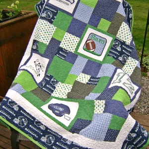 May include: A handmade quilt in shades of green, blue, and white, featuring a patchwork design with football-themed imagery. The quilt includes squares with football helmets, a football, and the word "Champions". The border is navy blue with football helmet patterns.