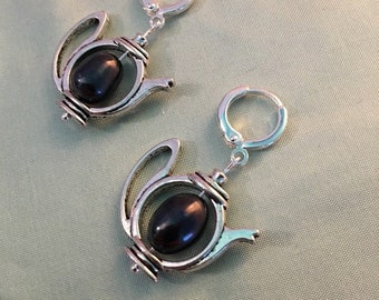 May include: A pair of silver teapot earrings with black gemstone accents. The earrings are dangling and have a hoop closure.