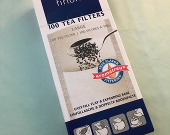 May include: A box of 100 large tea filters from the brand finum. The box is white with blue accents and features a picture of a tea bag in a spoon. The text on the box reads "100 Tea Filters", "Large", "100 Tee Filter / 100 Filtres a The", "True-Flavor aromatreu® Filtering", "Easy-Fill Flap & Expanding Base", and "Einfülltasche & Doppelte Bodenfalte".