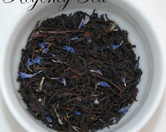 May include: A close-up of a bowl of loose leaf black tea with blue cornflower petals. The tea is called "Regency Tea" and the website is www.regencytea.com.