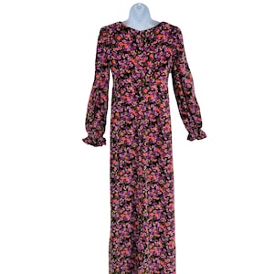May include: A long-sleeved floral dress with a black background and a pattern of pink, purple, and orange flowers. The dress has a round neckline, long sleeves with ruffled cuffs, and a button-down front. The dress is displayed on a white mannequin.