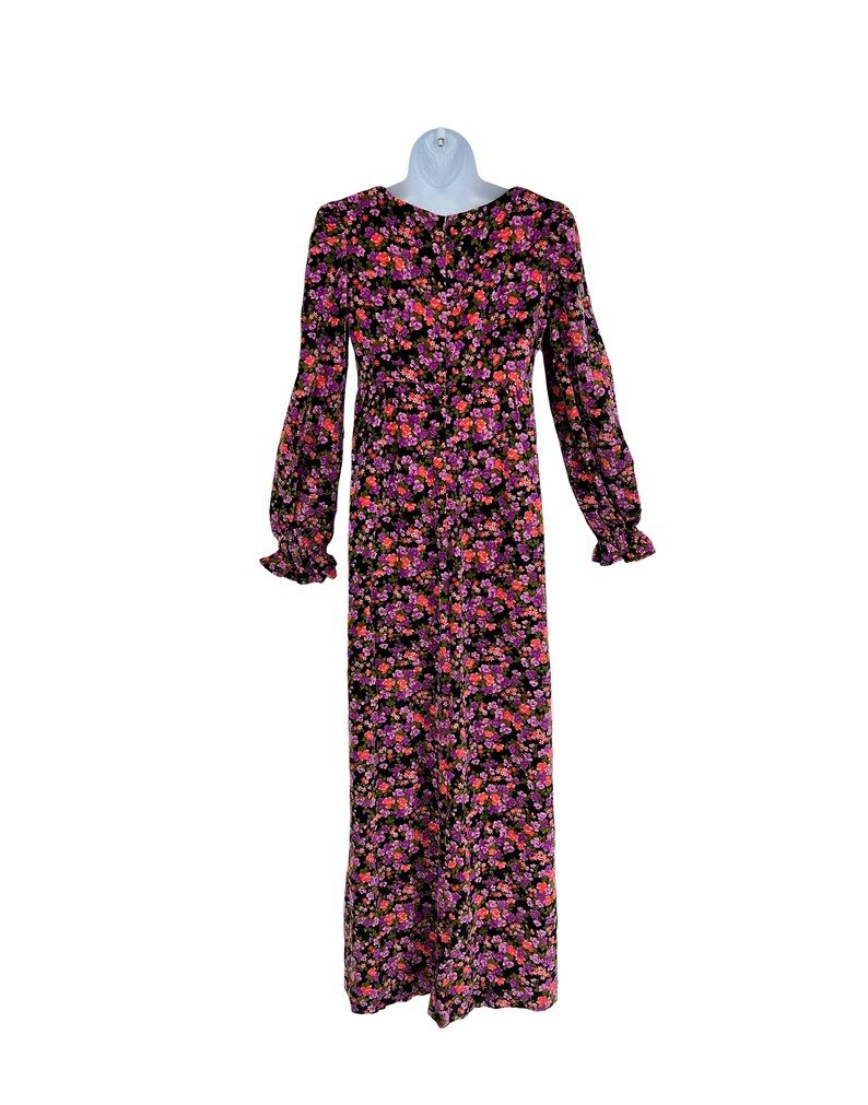 May include: A long-sleeved floral dress with a black background and a pattern of pink, purple, and orange flowers. The dress has a round neckline, long sleeves with ruffled cuffs, and a button-down front. The dress is displayed on a white mannequin.