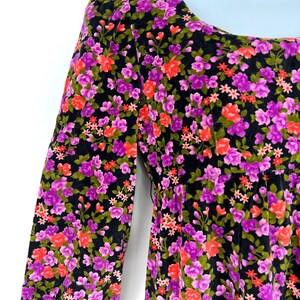 May include: A black floral dress with a scoop neckline and long sleeves. The dress features a vibrant pattern of pink, purple, and red flowers with green leaves. The fabric appears to be soft and has a slight sheen.