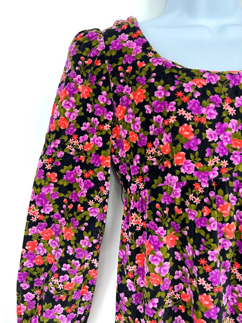 May include: A black floral dress with a scoop neckline and long sleeves. The dress features a vibrant pattern of pink, purple, and red flowers with green leaves. The fabric appears to be soft and has a slight sheen.