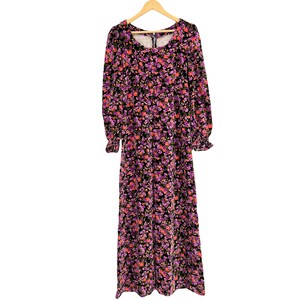 May include: A long-sleeved floral maxi dress with a scoop neckline and a zipper closure. The dress features a black background with a pattern of pink and purple flowers. The sleeves have ruffled cuffs, and the dress hangs on a wooden hanger.