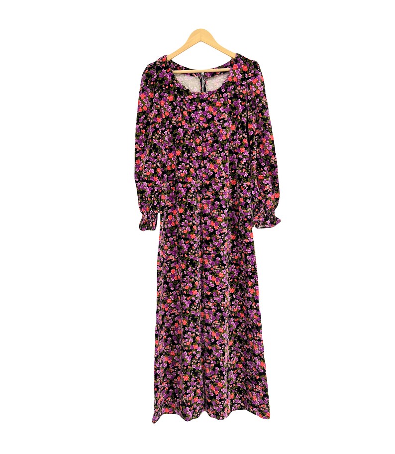 May include: A long-sleeved floral maxi dress with a scoop neckline and a zipper closure. The dress features a black background with a pattern of pink and purple flowers. The sleeves have ruffled cuffs, and the dress hangs on a wooden hanger.