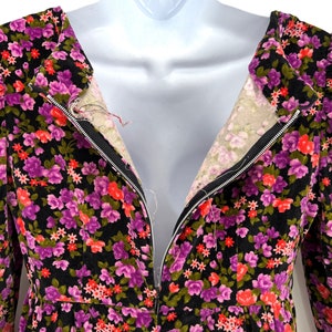 May include: A vintage floral dress with a black background and a vibrant pattern of purple, red, and green flowers. The dress features a zipper down the front and is displayed on a mannequin.