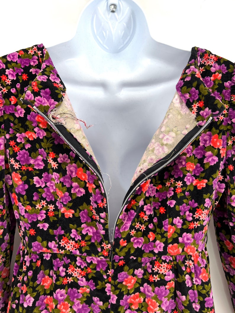 May include: A vintage floral dress with a black background and a vibrant pattern of purple, red, and green flowers. The dress features a zipper down the front and is displayed on a mannequin.