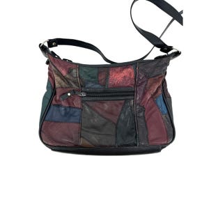 May include: A multi-colored patchwork shoulder bag constructed from various leather-like panels in shades of burgundy, black, dark blue, and forest green. The bag features a horizontal zippered front pocket, a black strap, and dark metal hardware.