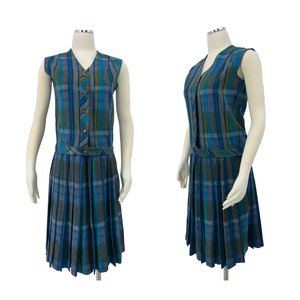 May include: A sleeveless plaid dress in shades of blue, gray, and green. The dress features a V-neck, button details, and a pleated skirt. The dress is displayed on a mannequin.