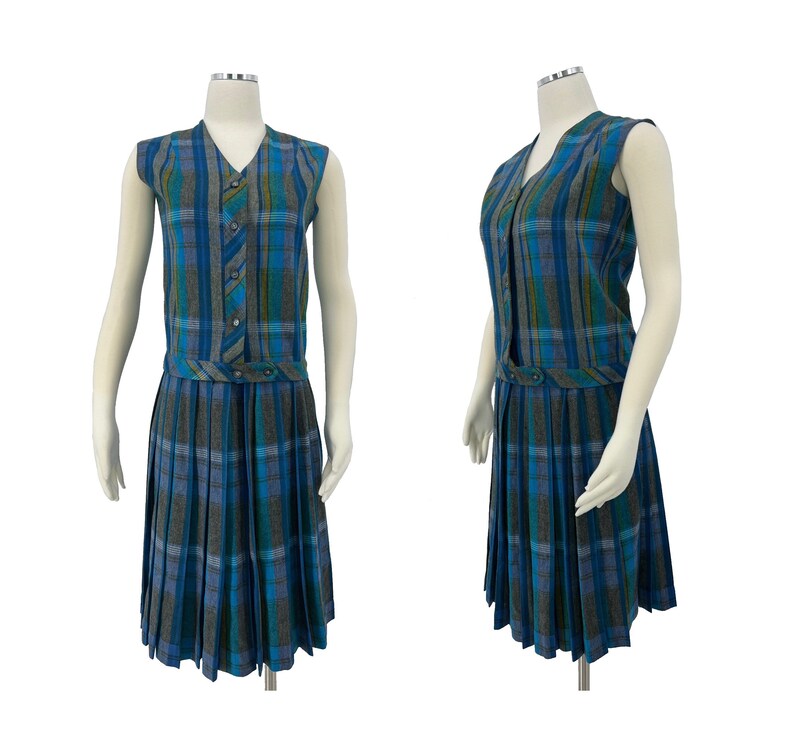 May include: A sleeveless plaid dress in shades of blue, gray, and green. The dress features a V-neck, button details, and a pleated skirt. The dress is displayed on a mannequin.