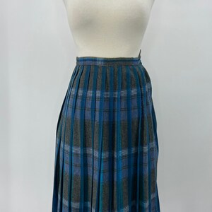 May include: A knee-length pleated skirt in a blue, gray, and teal plaid pattern. The skirt is displayed on a mannequin against a white background. The fabric has a textured appearance.