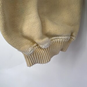 Op de afbeelding: Close-up van de cr&egrave;mekleurige geribbelde boord van een sweatshirt.