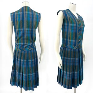 May include: A vintage plaid dress set in shades of blue, teal, and gray. The set includes a sleeveless, button-down vest and a pleated skirt. The vest has a V-neck and a matching belt detail at the waist. The skirt falls to the knee.