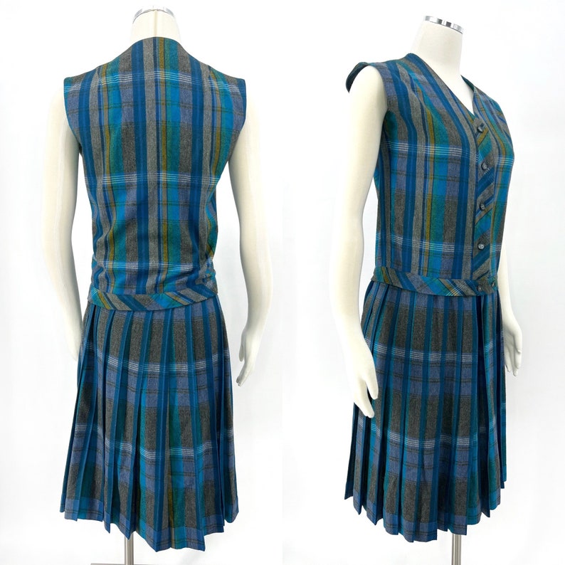 May include: A vintage plaid dress set in shades of blue, teal, and gray. The set includes a sleeveless, button-down vest and a pleated skirt. The vest has a V-neck and a matching belt detail at the waist. The skirt falls to the knee.