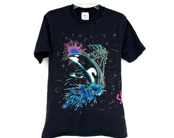 May include: Black t-shirt with a graphic print of three orcas jumping out of the water with fireworks in the background. The text "Sea World" is printed on the shirt.