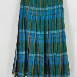 May include: A pleated skirt with a plaid pattern in shades of blue, green, and gold. The skirt is hanging on a wooden hanger against a white background. The fabric appears to be a wool blend.