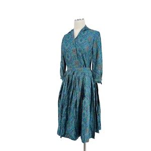 May include: A blue and green patterned dress with a collared neckline and long sleeves. The dress has a fitted bodice and a full skirt.