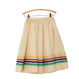 May include: A cream-colored skirt with a rainbow-colored stripe around the bottom. The skirt is hanging on a wooden hanger.